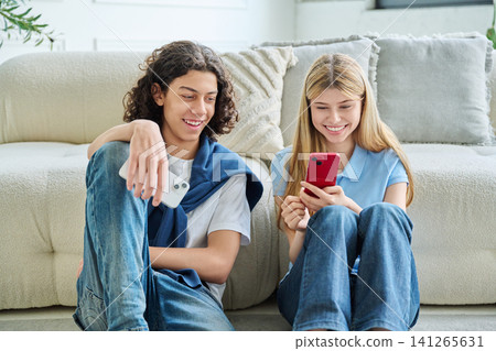 Teenage boy and girl using smartphones together while sitting on floor Teenage boy and girl using smartphones together while sitting on floor 141265631