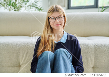 Smiling teenage student girl in glasses sitting on floor hugging knees. Smiling teenage student girl in glasses sitting on floor hugging knees. 141265635