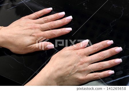 Receiving Professional Manicure in Modern Salon. Beautiful, well-groomed women's hands with elegant nails against a dark background. Beauty salon concept: manicures, pedicures. Receiving Professional Manicure in Modern Salon. Beautiful, well-groomed women's hands with elegant nails against a dark background. Beauty salon concept: manicures, pedicures. 141265658