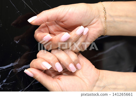 Receiving Professional Manicure in Modern Salon. Beautiful, well-groomed women's hands with elegant nails against a dark background. Beauty salon concept: manicures, pedicures. 141265661