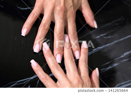 Receiving Professional Manicure in Modern Salon. Beautiful, well-groomed women's hands with elegant nails against a dark background. Beauty salon concept: manicures, pedicures. Receiving Professional Manicure in Modern Salon. Beautiful, well-groomed women's hands with elegant nails against a dark background. Beauty salon concept: manicures, pedicures. 141265664