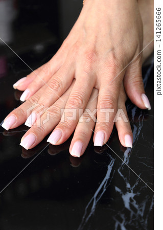 Receiving Professional Manicure in Modern Salon. Beautiful, well-groomed women's hands with elegant nails against a dark background. Beauty salon concept: manicures, pedicures. Receiving Professional Manicure in Modern Salon. Beautiful, well-groomed women's hands with elegant nails against a dark background. Beauty salon concept: manicures, pedicures. 141265666