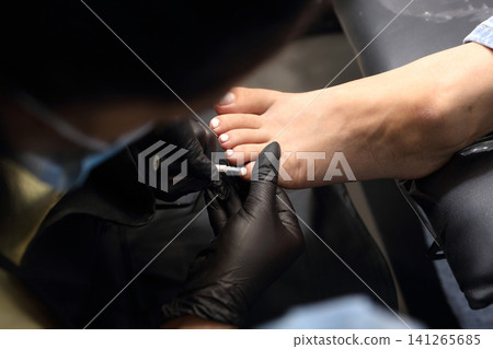 A woman's feet during a pedicure. Woman getting pedicure in beauty salon, closeup. A pedicurist working at a beauty salon. Manicure services. Nail art. Beauty salon concept: pedicures. 141265685
