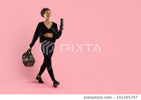 Black woman walking with gym bag and reusable bottle and looking aside 141265747