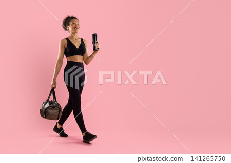 Smiling Black woman in sportswear walking with gym bag and reusable bottle Smiling Black woman in sportswear walking with gym bag and reusable bottle 141265750