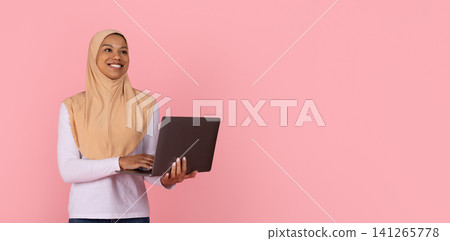 Smiling young Black Muslim woman in beige hijab working on open laptop Smiling young Black Muslim woman in beige hijab working on open laptop 141265778