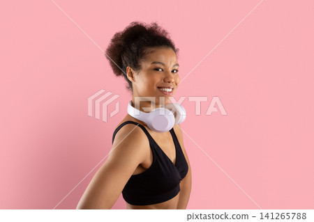 Smiling young Black woman in activewear with wireless headphones around neck Smiling young Black woman in activewear with wireless headphones around neck 141265788
