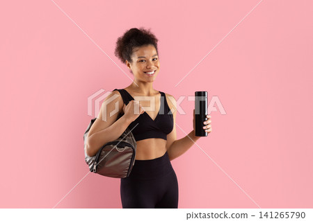 Portrait of smiling young Black woman holding gym bag and water bottle Portrait of smiling young Black woman holding gym bag and water bottle 141265790