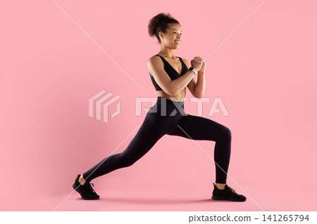 Smiling young Black fitness woman in activewear performing forward lunge Smiling young Black fitness woman in activewear performing forward lunge 141265794