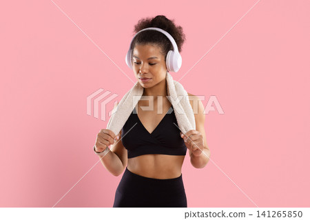 Black woman in workout clothes and wireless headphones holding towel after exercise Black woman in workout clothes and wireless headphones holding towel after exercise 141265850