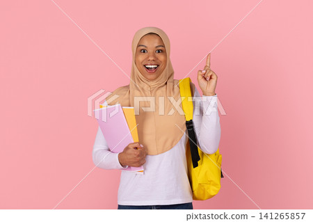 Black female student in hijab holding notebooks and raising finger, having idea Black female student in hijab holding notebooks and raising finger, having idea 141265857