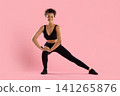 Smiling young Black woman performing side lunge stretch in activewear 141265876
