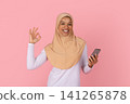 Black Muslim woman in hijab holding smartphone and making approval ok gesture 141265878