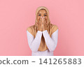 Surprised Black Muslim woman in beige hijab covering her mouth with hands 141265883