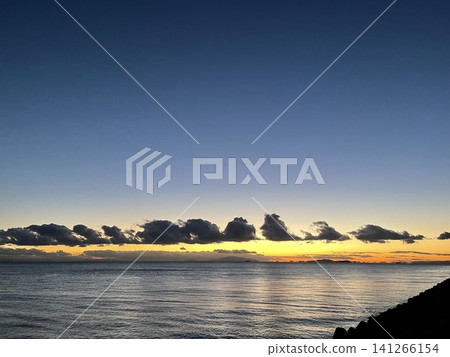 夕陽西下，地平線上排列著朵朵白雲，海面平靜無波。 141266154