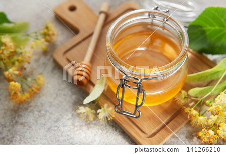 Fresh linden honey jar with blooming flowers Fresh linden honey jar with blooming flowers 141266210