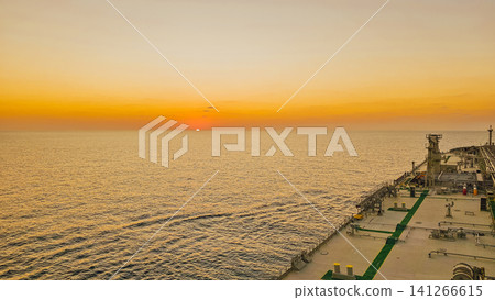 Horizontal high angle view of a golden sunset over the calm ocean taken from the deck of a large merchant cargo ship sailing during a quiet evening at sea Horizontal high angle view of a golden sunset over the calm ocean taken from the deck of a large merchant cargo ship sailing during a quiet evening at sea 141266615