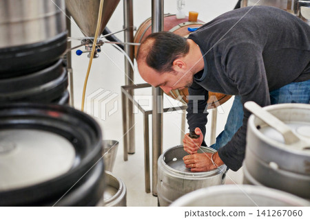 Brewery, man and kegs machine with manufacturing for craft beer, alcohol and production process in factory. Industrial industry, worker and working in distillery with tank for brewing in warehouse Brewery, man and kegs machine with manufacturing for craft beer, alcohol and production process in factory. Industrial industry, worker and working in distillery with tank for brewing in warehouse 141267060