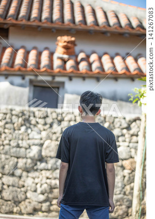 A boy looks up at the traditional red tiled roofs and Shisa statues of Okinawa. A boy looks up at the traditional red tiled roofs and Shisa statues of Okinawa. 141267083