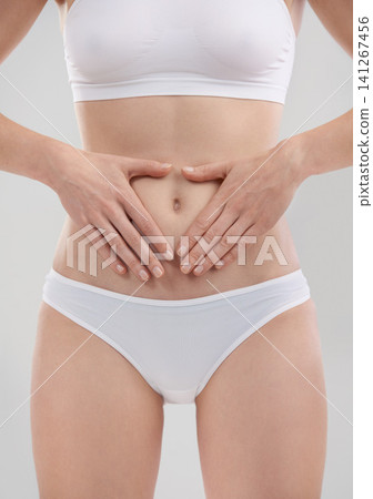 Woman, hands and stomach for wellness in studio, heart and body for diet and holistic gut health. Digestion, weight loss and abdomen detox for female person, self care for balance on background Woman, hands and stomach for wellness in studio, heart and body for diet and holistic gut health. Digestion, weight loss and abdomen detox for female person, self care for balance on background 141267456