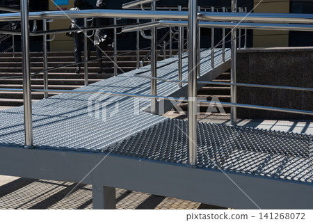 A Detailed View of a Modern Accessibility Ramp Featuring Metal Grating and Handrails Leading to an Urban Building A Detailed View of a Modern Accessibility Ramp Featuring Metal Grating and Handrails Leading to an Urban Building 141268072