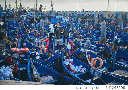 Colorful blue fishing boats crowded in Essaouira harbor, Morocco, authentic coastal fishing scene Colorful blue fishing boats crowded in Essaouira harbor, Morocco, authentic coastal fishing scene 141268508