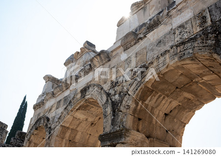 Marvel at the stunning architecture of Pamukkales ancient ruins, where visitors enjoy the rich history and natural beauty beneath the sunny sky. 141269080