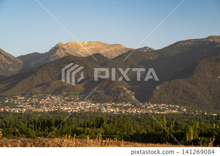 Golden sunlight casts a warm glow over a town surrounded by majestic mountains, showcasing natures beauty at dusk with clear skies. Golden sunlight casts a warm glow over a town surrounded by majestic mountains, showcasing natures beauty at dusk with clear skies. 141269084