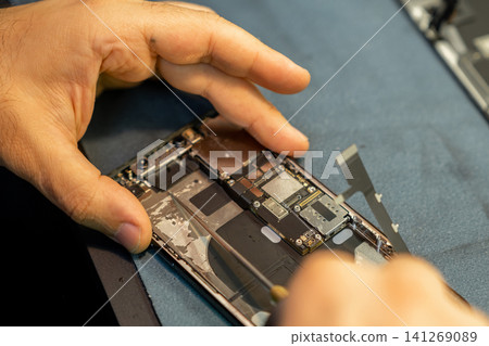 Technician skillfully disassembles a smartphone to replace internal components in a clean and organized repair workshop during daylight hours. Technician skillfully disassembles a smartphone to replace internal components in a clean and organized repair workshop during daylight hours. 141269089