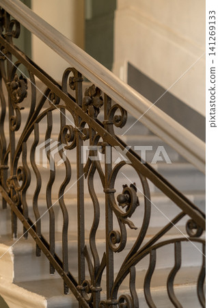 Intricate wrought iron railing showcases its detailed craftsmanship along the elegant stairway in a refined building, enhancing the overall ambiance and style. Intricate wrought iron railing showcases its detailed craftsmanship along the elegant stairway in a refined building, enhancing the overall ambiance and style. 141269133