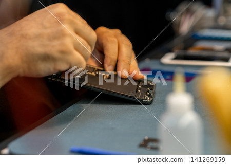 Technician skillfully disassembles a smartphone in a workshop setting, focusing on intricate parts while utilizing specialized tools for repair tasks. Technician skillfully disassembles a smartphone in a workshop setting, focusing on intricate parts while utilizing specialized tools for repair tasks. 141269159