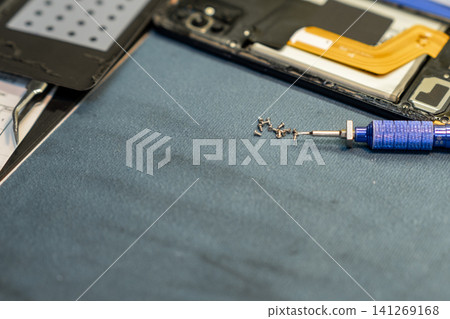 Screws and tools are organized neatly on a work surface while a technician focuses on the intricate details of phone repair in a shop. Screws and tools are organized neatly on a work surface while a technician focuses on the intricate details of phone repair in a shop. 141269168