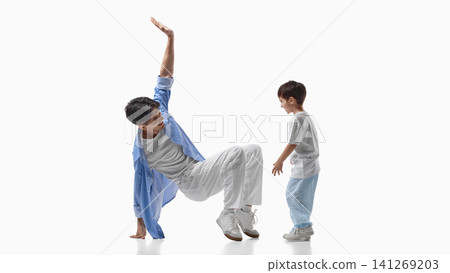 Father performing playful dance move while son watches in studio. 141269203
