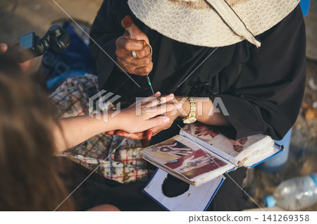 Henna artist painting a tourist's hand in Essaouira Morocco capturing authentic culture and tradition Henna artist painting a tourist's hand in Essaouira Morocco capturing authentic culture and tradition 141269358