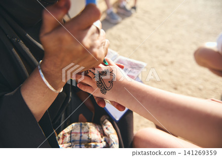 Henna artist decorating tourist's hand with heart design in Essaouira Morocco market Henna artist decorating tourist's hand with heart design in Essaouira Morocco market 141269359