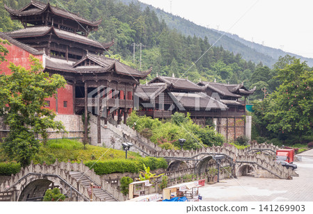 Traditional wooden Miao ethnic minority architecture and pavilions nestled against a lush green hillside at Chiyou Jiuli City complex in Pengshui, Chongqing, China. Traditional wooden Miao ethnic minority architecture and pavilions nestled against a lush green hillside at Chiyou Jiuli City complex in Pengshui, Chongqing, China. 141269903