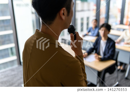 The instructor speaks with a microphone, and the participants listen. 141270353