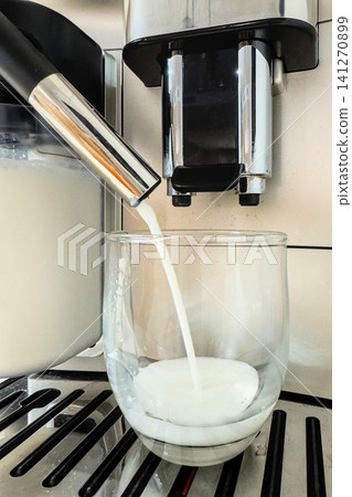 Fresh milk pours from a coffee machine into a clear glass for a latte macchiato. Making a layered milk coffee at home Fresh milk pours from a coffee machine into a clear glass for a latte macchiato. Making a layered milk coffee at home 141270899