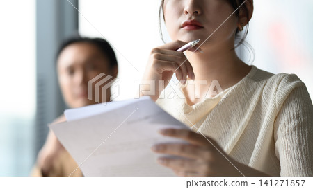 A woman deep in thought, holding documents in her hand. 141271857