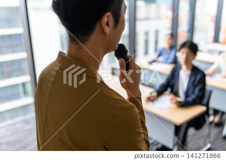 A male instructor holding a microphone and the students A male instructor holding a microphone and the students 141271866