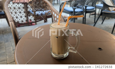 An iced cafe latte with foam, served in a large glass with two orange straws, sitting on an outdoor cafe table An iced cafe latte with foam, served in a large glass with two orange straws, sitting on an outdoor cafe table 141272638