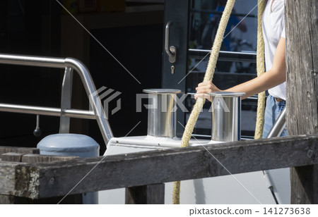 Person holding a yellow braided rope on a boat dock, illustrating nautical lifestyle in a casual marina setting. Person holding a yellow braided rope on a boat dock, illustrating nautical lifestyle in a casual marina setting. 141273638