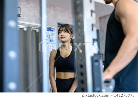 一位年輕女子在健身房接受教練指導使用器材;一位女子正在鍛鍊;正面視角。 一位年輕女子在健身房接受教練指導使用器材;一位女子正在鍛鍊;正面視角。 141273773
