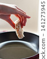 A close-up of hands frying croquettes in oil in a pot. 141273945