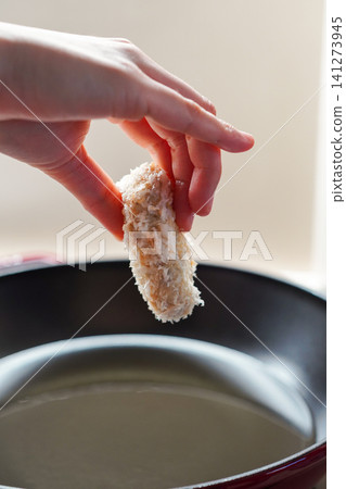 A close-up of hands frying croquettes in oil in a pot. 141273945
