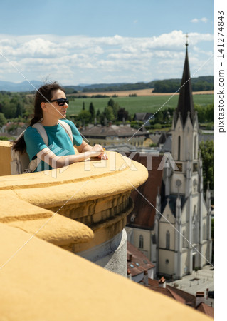 Young woman tourist with backpack enjoying panorama of the old Austrian historical city. Young woman tourist with backpack enjoying panorama of the old Austrian historical city. 141274843