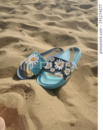 Beach slippers with daisies on the sand on a sunny day Beach slippers with daisies on the sand on a sunny day 141274877