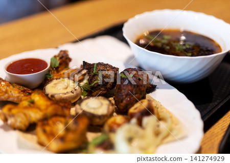Grilled mixed meat and seafood platter with vegetables and dipping sauces on wooden table under warm light, styled for casual dining with rich char, fresh garnish, and inviting color Grilled mixed meat and seafood platter with vegetables and dipping sauces on wooden table under warm light, styled for casual dining with rich char, fresh garnish, and inviting color 141274929