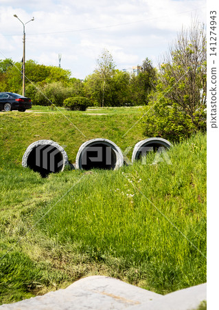 Concrete culvert pipes in grassy roadside ditch under daylight sky Concrete culvert pipes in grassy roadside ditch under daylight sky 141274943