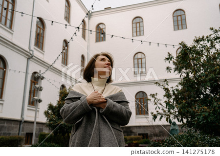 Woman stands in a courtyard with string lights near a building during daylight hours Woman stands in a courtyard with string lights near a building during daylight hours 141275178